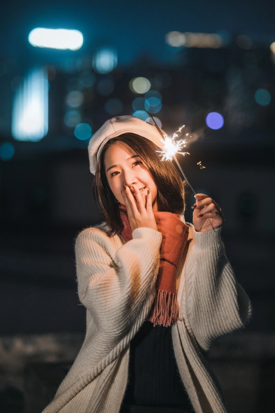 夜晚戴帽子的年轻女子手持点燃的焰火