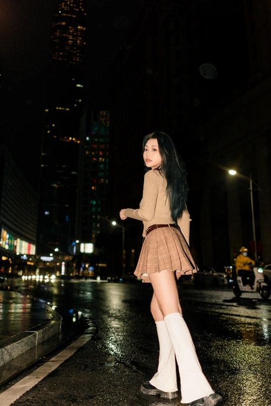 一位穿着过膝靴和带着伞的年轻女子在夜晚的城市街道上行走。