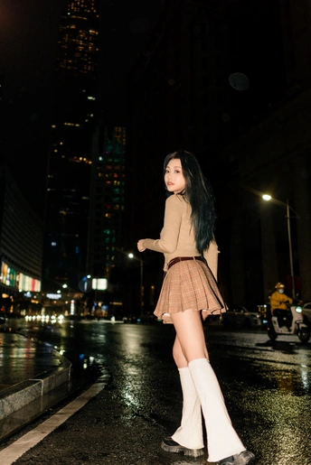 一位穿着过膝靴和带着伞的年轻女子在夜晚的城市街道上行走。