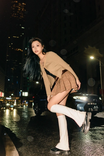 一个穿高筒靴和带着雨伞的年轻女子在夜晚的城市街道上摆姿势