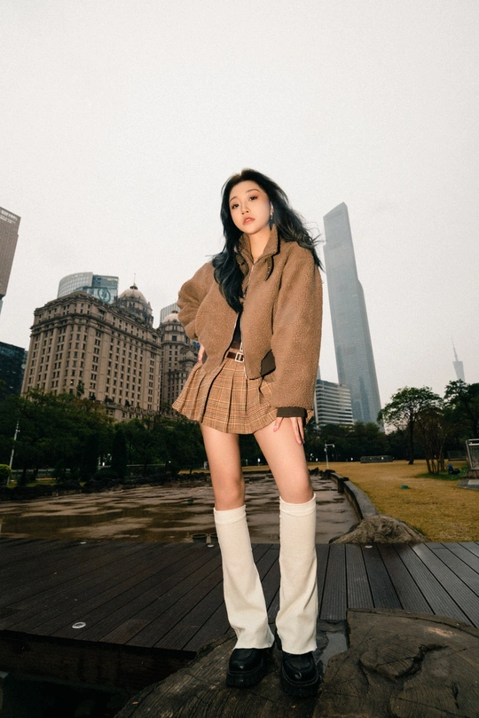 一位穿着棕色外套和高筒靴子的女性站在高楼前