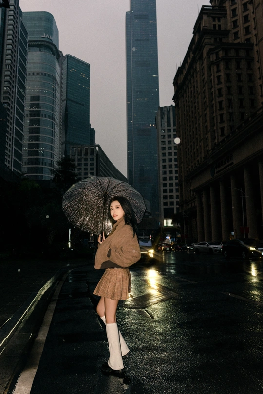 一位年轻女子手持雨伞站在城市街道上 背景是建筑物