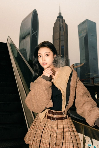 一位穿着格子裙子的年轻女子在有摩天大楼作背景的自动扶梯上为拍照姿势 