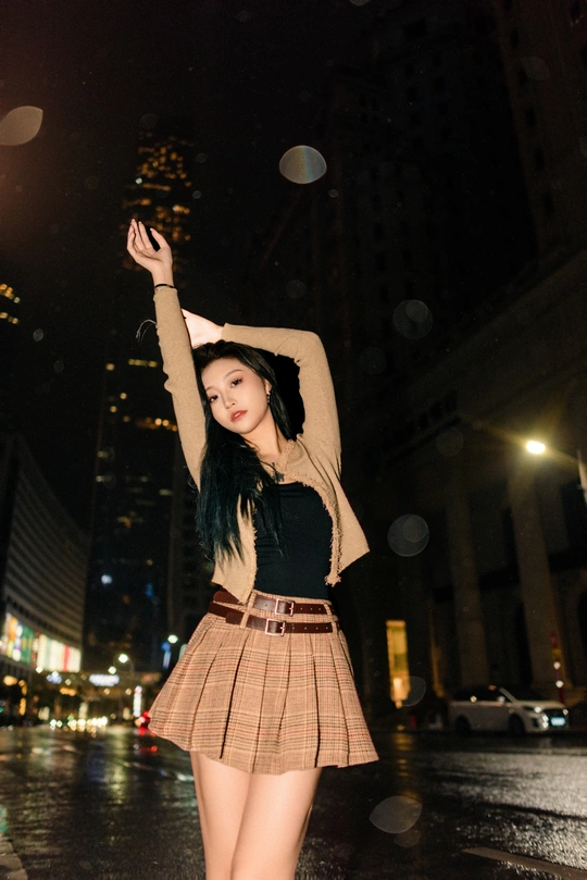 一位穿着裙子的年轻女子在夜晚的城市中站在雨中