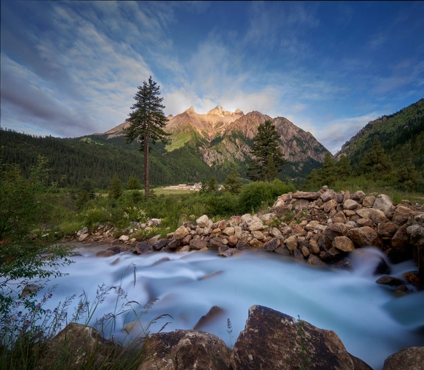 夕阳下有岩石和树木的河流背景 远处有山脉。