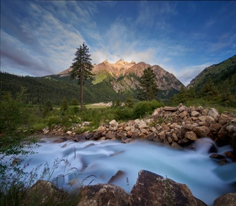 夕阳下有岩石和树木的河流背景 远处有山脉。