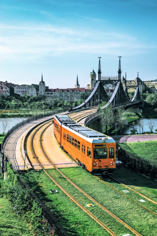 一辆橙色的旅客列车在靠近桥和河的铁路轨道上行驶。