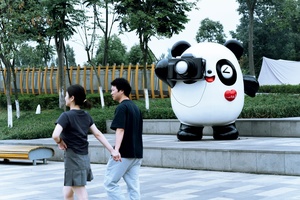 一个人和一个年轻男孩走过公园里一只大熊猫的大型雕像。