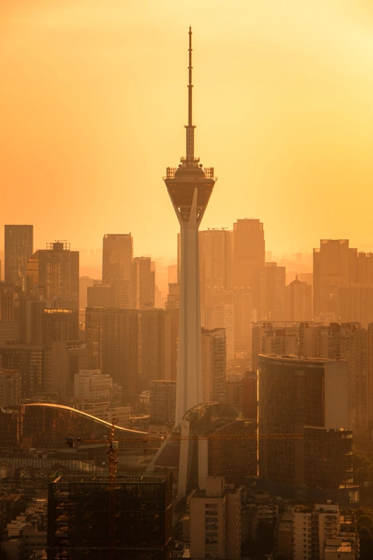 夕阳下 太阳落在一个城市上 前景中有一座高塔。