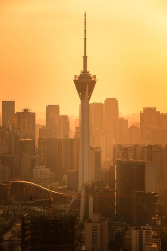 夕阳下 太阳落在一个城市上 前景中有一座高塔。