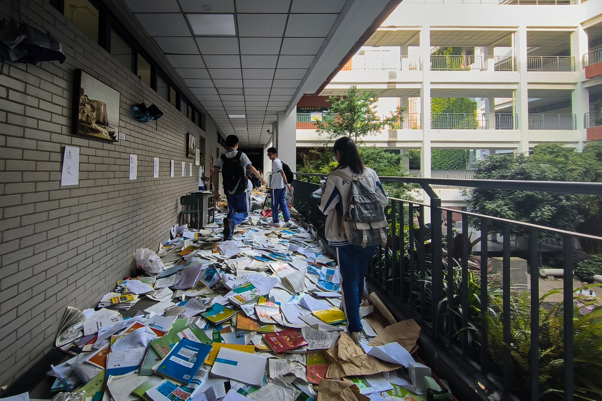 人们走过一栋建筑的走廊 墙壁上有垃圾 阳台上堆满了书。