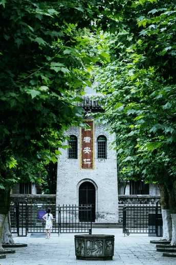 一个小女孩站在一栋建筑前 周围有树木和长凳。