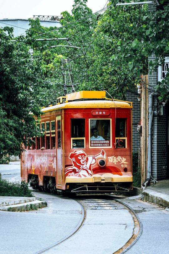 一辆红色和黄色的手推车上有涂鸦 停在旁边有树木和建筑物的轨道上。