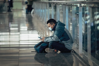 一个戴口罩的男子坐在机场地板上