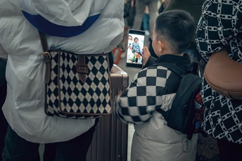 站在一名女子旁边的一名男子正在给一名站在一名男孩旁边的人拍照 男孩正在看他的手机。