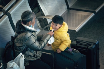 一个年轻的儿童坐在一位妇女旁边 这位妇女站在行李旁边。