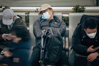 一个戴口罩的男子坐在地铁的长椅上 正在看手机。