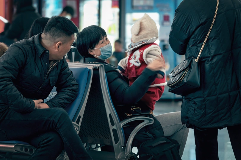 一位抱着婴儿坐在长凳上的男人 旁边站着一位女人。