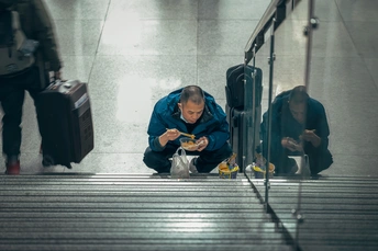 一个坐在楼梯地板上的男人带着一个行李袋 另一个男人跪在地上看着他的手机。