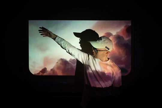 一个戴帽子的人在窗户前站立 双手伸开 一个女性站在他身后。