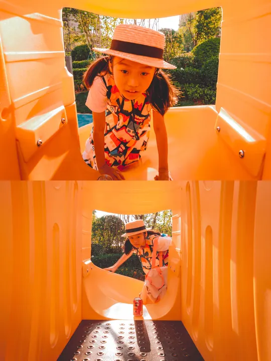 一个戴帽子的小女孩在游乐场的一个黄色滑梯里玩耍