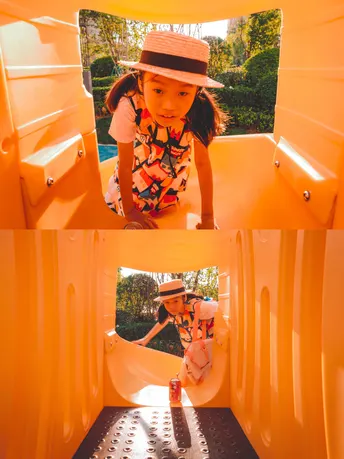 一个戴帽子的小女孩在游乐场的一个黄色滑梯里玩耍