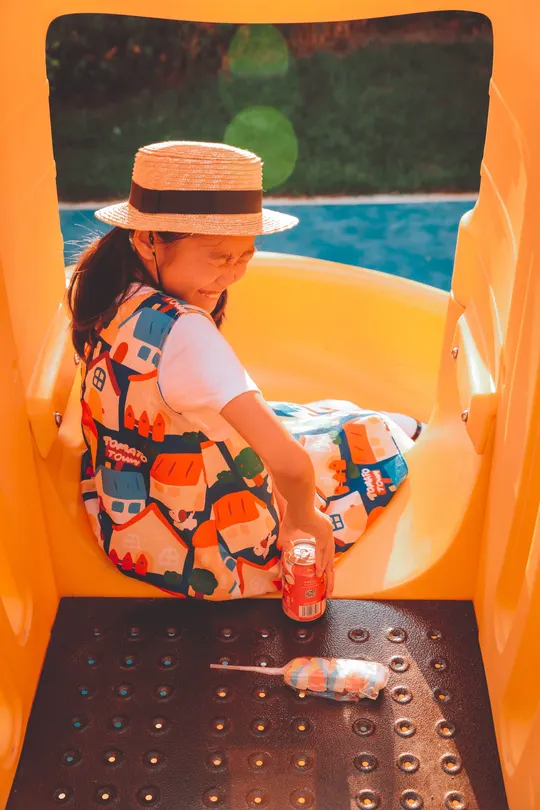 一个戴帽子的女孩坐在游乐场的小滑梯顶部