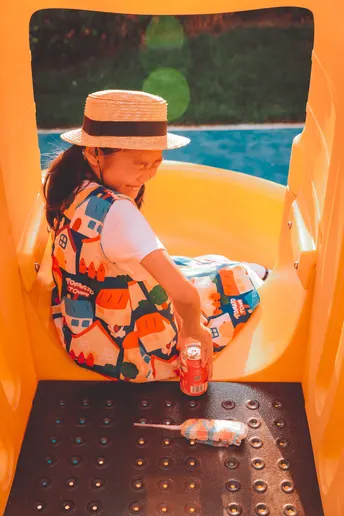 一个戴帽子的女孩坐在游乐场的小滑梯顶部