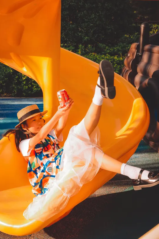 一个小女孩在公园里滑下了一个黄色的滑梯。