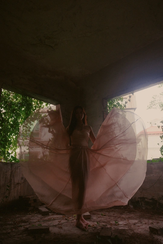 一个穿着粉红色连衣裙的女孩拿着雨伞站在一座废弃的建筑中