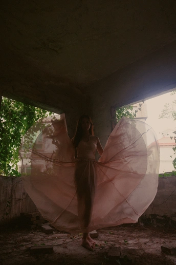 一个穿着粉红色连衣裙的女孩拿着雨伞站在一座废弃的建筑中