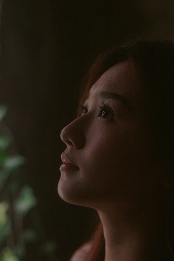 一个年轻女子在窗前凝视着一盆植物的阴暗肖像