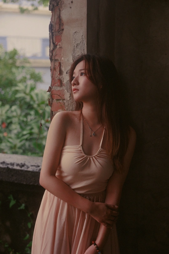 一位穿着粉红色连衣裙的美丽年轻女子靠在墙上 正在透过窗户向外看。