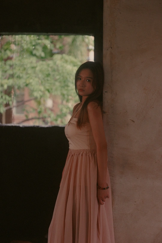 一位穿着粉红色连衣裙的年轻女子站在窗户前