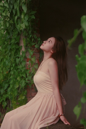 一个穿粉色连衣裙的年轻女子坐在墙边的常春藤前。