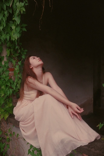 一个美丽的年轻女子穿着白色连衣裙坐在石头边缘