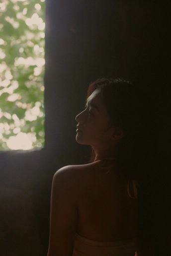 一个穿着连衣裙的年轻女子站在一个光线昏暗的房间里 背景中有一棵树。