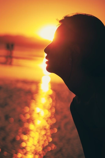 一位女性在海滩上凝视着夕阳下的海洋轮廓