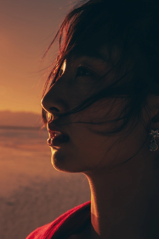 一个年轻女子站在夕阳下的海滩上 面带微笑 眺望着海洋。