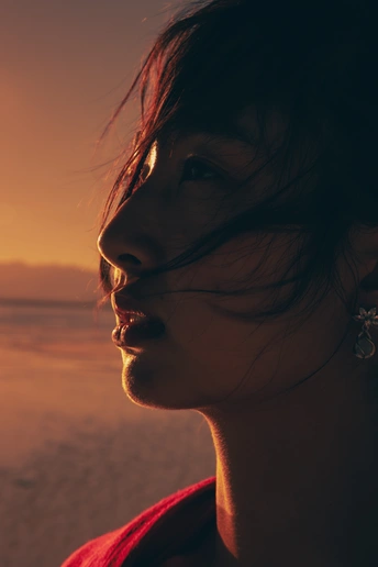 一个年轻女子站在夕阳下的海滩上 面带微笑 眺望着海洋。