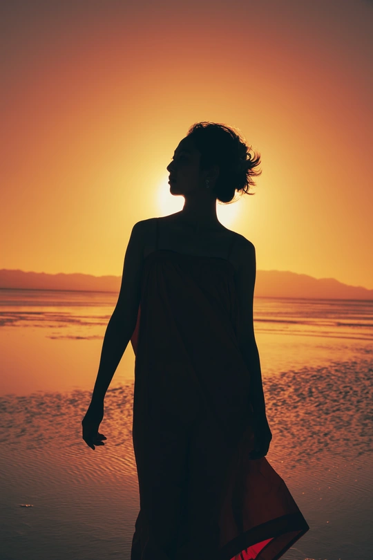 夕阳西下 海面上的沙滩上 一位穿着连衣裙的年轻女子剪影。