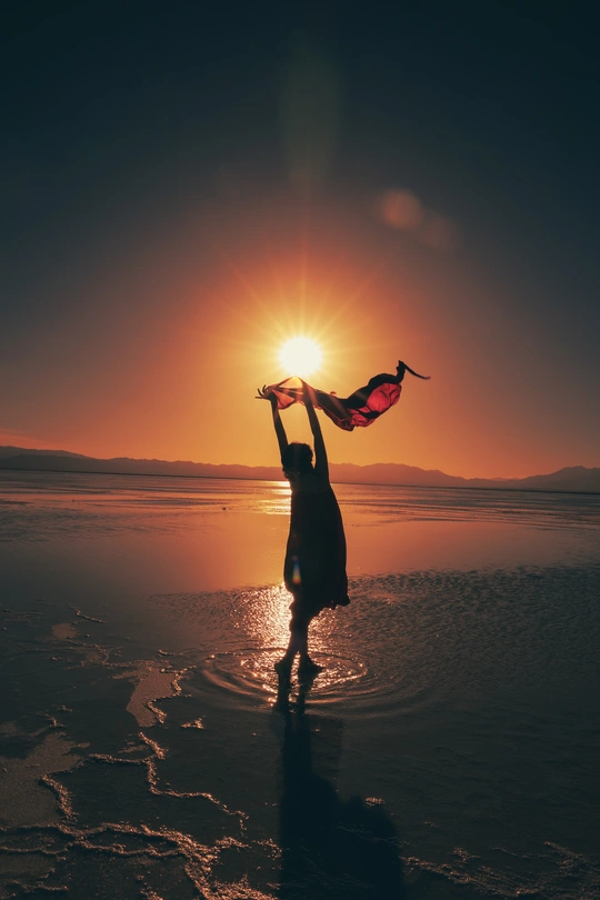 夕阳下 一个年轻女子站在沙滩上 手里拿着一条围巾。