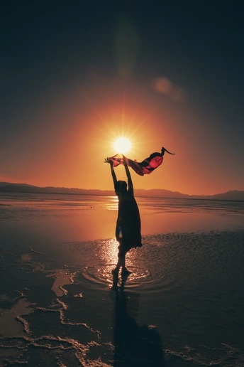 夕阳下 一个年轻女子站在沙滩上 手里拿着一条围巾。