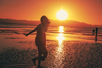 夕阳下 一位年轻女子在海滩上奔跑的剪影