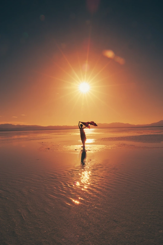 一位站在水边 手臂伸展在夕阳或日出时分的海滩上的女人