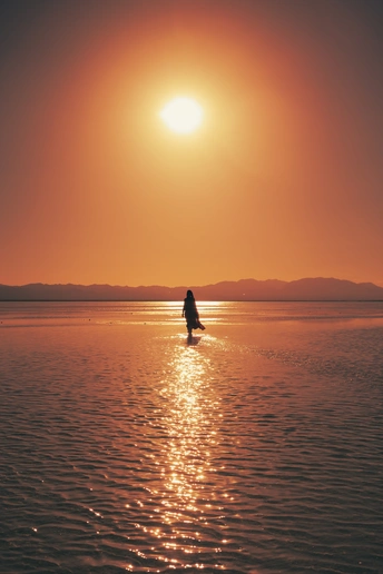 一个人站在一艘船上一片水域中 当太阳落山时