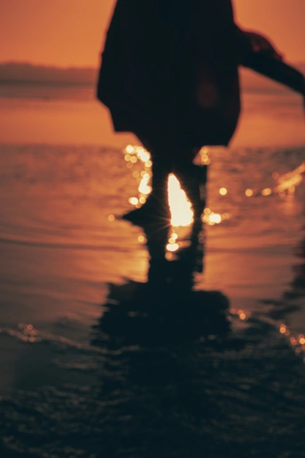 夕阳下在海滩上行走的女人剪影 双脚浸在水中