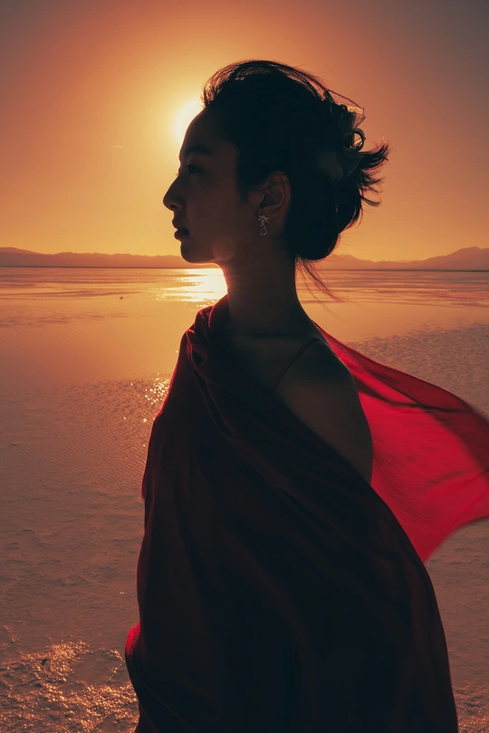 一位戴红披肩的女人站在海滩上 当夕阳西下时 夕阳洒在海洋上。