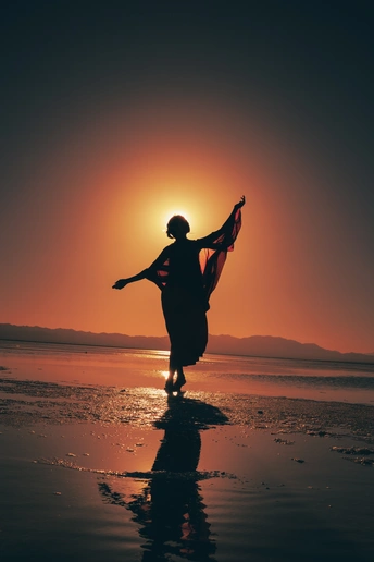 夕阳下穿着连衣裙和围巾的年轻美女在海滩上的剪影