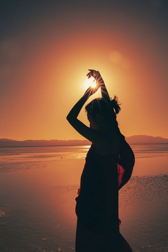 一位年轻女子在海滩上 当太阳落山时 她把头高高举起 轮廓显得非常美丽。